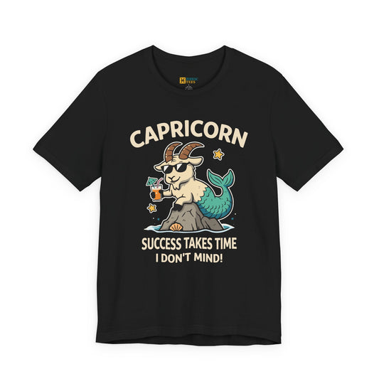 Capricorn zodiac T-shirt with cartoon sea-goat character sitting on a rock, wearing sunglasses and holding a drink, text reads “Success Takes Time, I Don’t Mind.