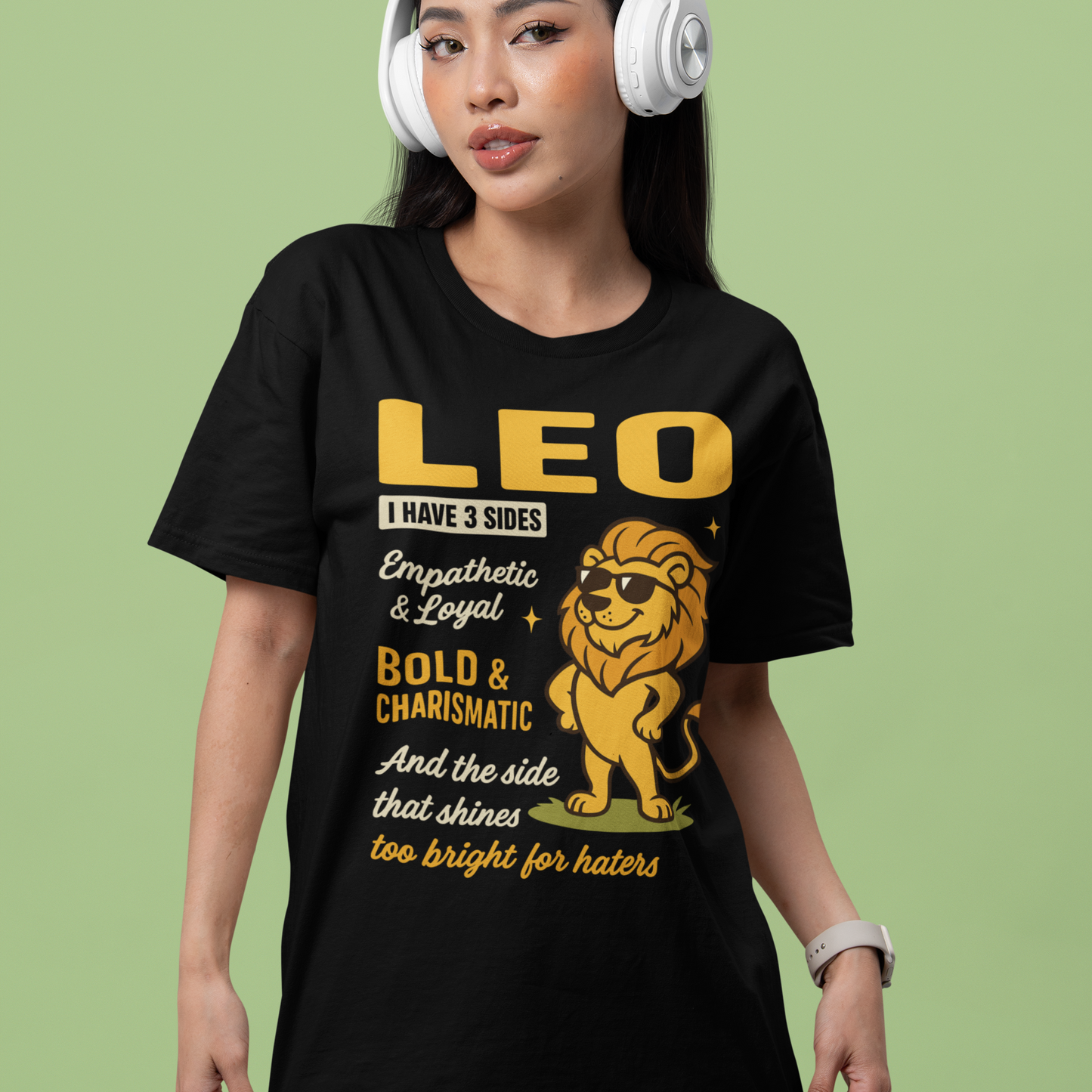Woman wearing a black Leo astrology T-shirt with bold yellow text and a cartoon lion, posing casually in front of a light green background.