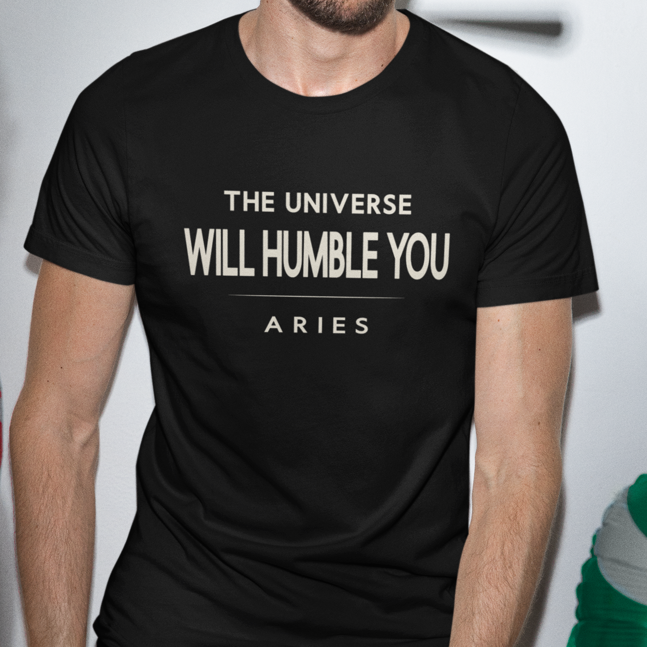 Model wearing Aries zodiac t-shirt with “The Universe Will Humble You” bold typography quote design