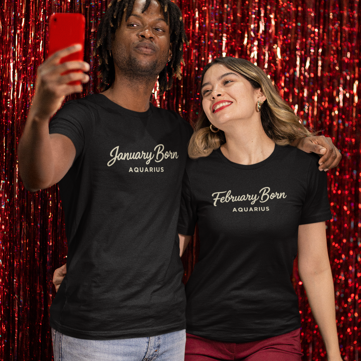 A woman wearing a black February Born Aquarius T-shirt smiles happily while posing for a selfie with a man in front of a sparkly party backdrop.