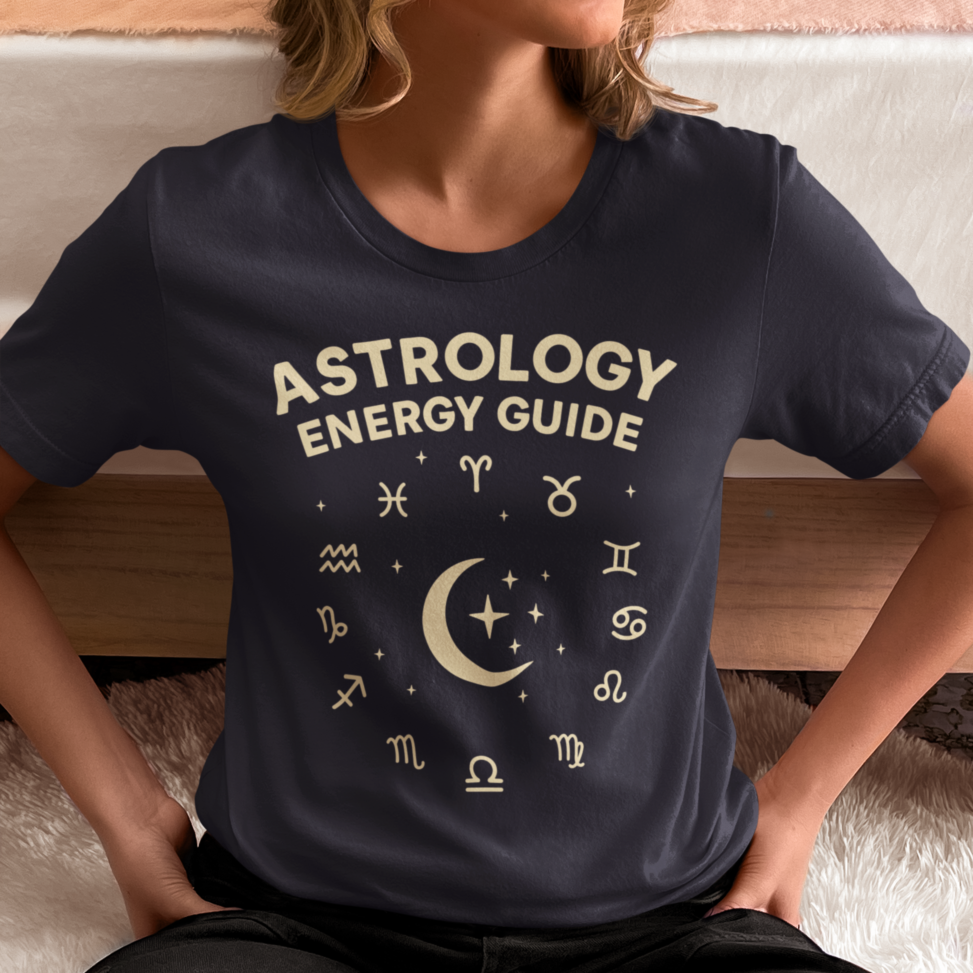 Woman wearing an Astrology Energy Guide T-shirt featuring zodiac symbols and a moon graphic while sitting casually indoors